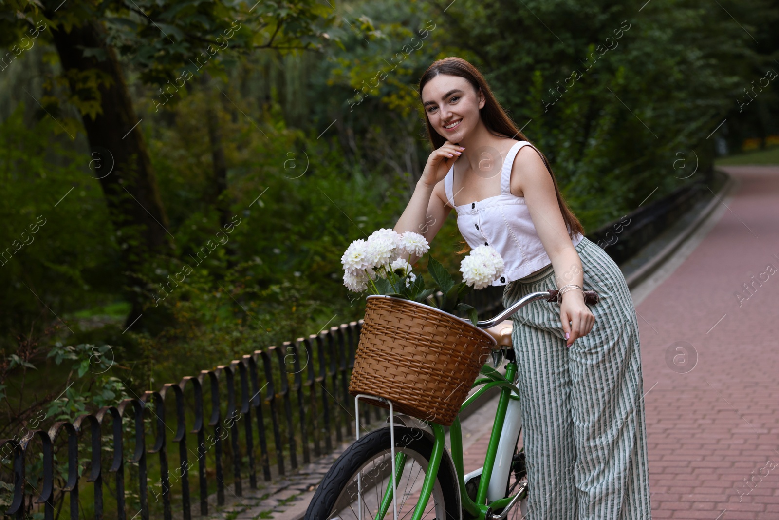 Photo of Woman walking her bicycle with flowers in basket outdoors. Space for text