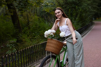 Photo of Woman walking her bicycle with flowers in basket outdoors. Space for text