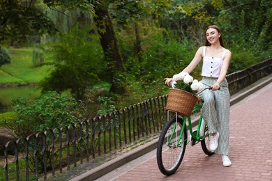 Photo of Woman walking her bicycle with flowers in basket outdoors. Space for text