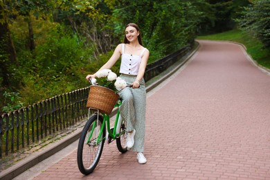Photo of Woman walking her bicycle with flowers in basket outdoors. Space for text