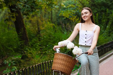 Photo of Woman walking her bicycle with flowers in basket outdoors. Space for text