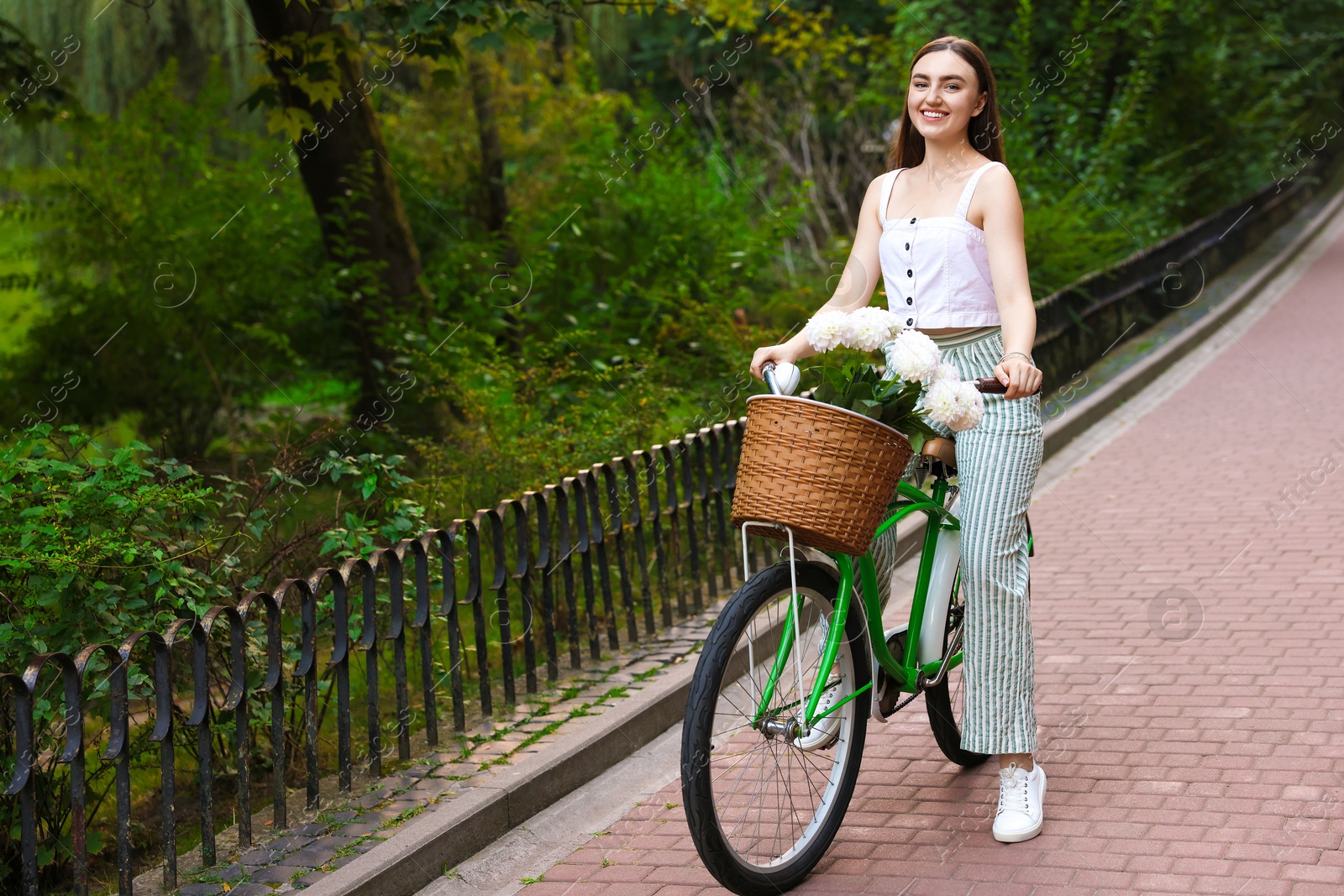 Photo of Woman riding bicycle with flowers in basket outdoors. Space for text
