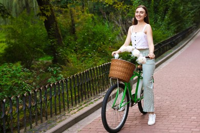 Photo of Woman riding bicycle with flowers in basket outdoors. Space for text