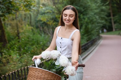 Photo of Woman riding bicycle with flowers in basket outdoors