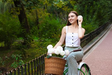 Photo of Woman riding bicycle with flowers in basket outdoors. Space for text