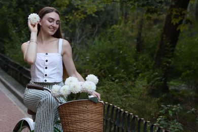 Photo of Woman riding bicycle with flowers in basket outdoors. Space for text