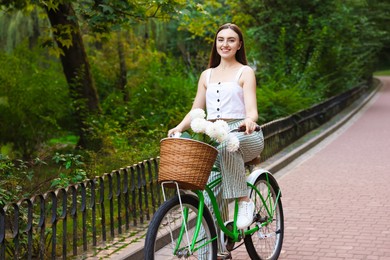Photo of Woman riding bicycle with flowers in basket outdoors
