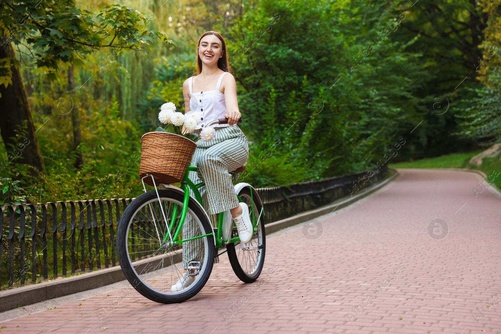Photo of Woman riding bicycle with flowers in basket outdoors. Space for text