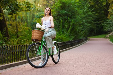 Photo of Woman riding bicycle with flowers in basket outdoors. Space for text