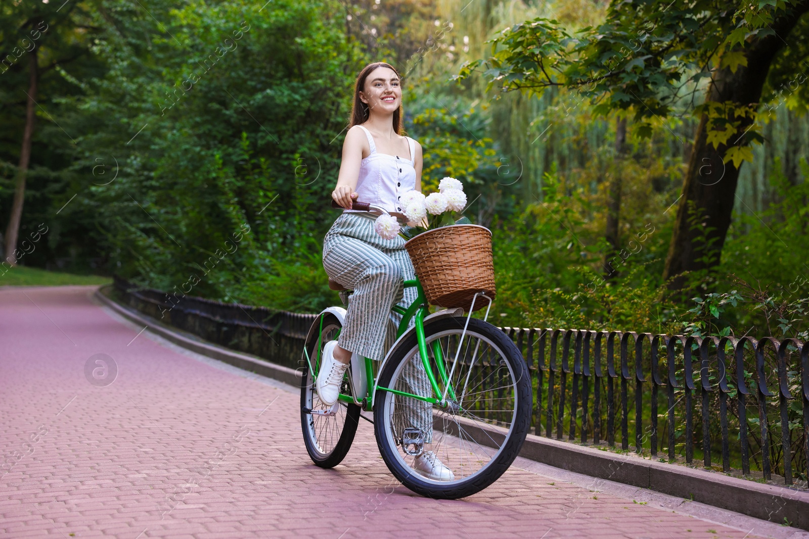Photo of Woman riding bicycle with flowers in basket outdoors