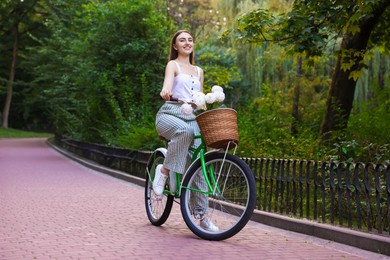 Photo of Woman riding bicycle with flowers in basket outdoors