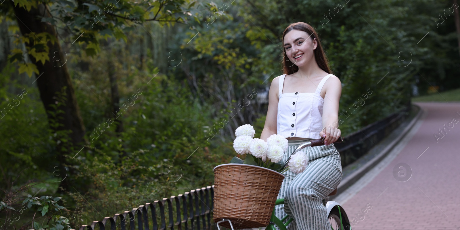 Photo of Woman riding bicycle with flowers in basket outdoors. Space for text