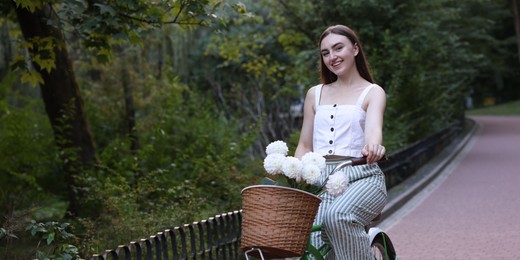 Photo of Woman riding bicycle with flowers in basket outdoors. Space for text