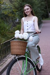 Photo of Woman riding bicycle with flowers in basket outdoors