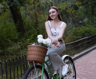 Photo of Woman riding bicycle with flowers in basket outdoors