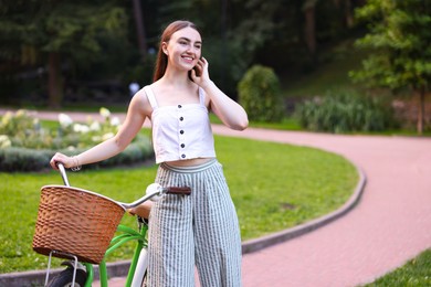 Photo of Happy woman walking bicycle in park. Space for text