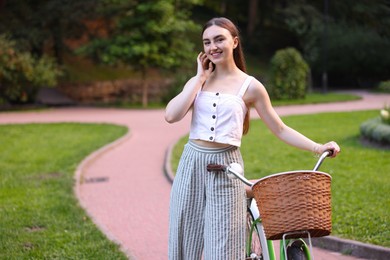 Photo of Happy woman walking bicycle in park. Space for text