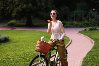 Photo of Happy woman blowing air kiss while riding bicycle in park
