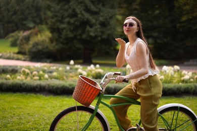 Photo of Happy woman blowing air kiss while riding bicycle in park. Space for text