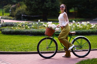 Photo of Woman riding bicycle with flowers in basket outdoors. Space for text