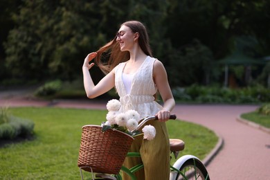 Photo of Woman riding bicycle with flowers in basket outdoors