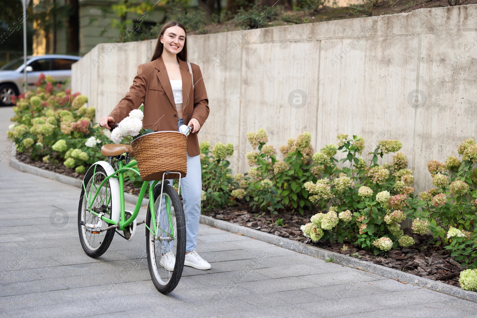 Photo of Woman walking her bicycle with flowers in basket outdoors. Space for text
