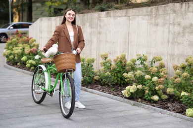 Photo of Woman walking her bicycle with flowers in basket outdoors. Space for text