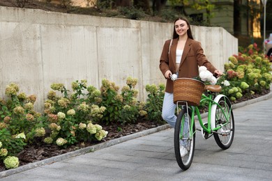 Photo of Woman walking her bicycle with flowers in basket outdoors. Space for text