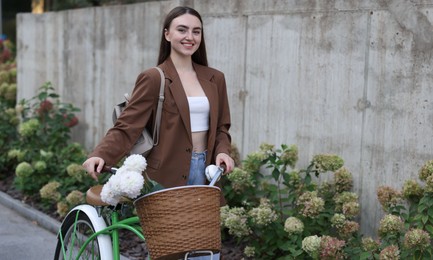 Photo of Woman walking her bicycle with flowers in basket outdoors. Space for text