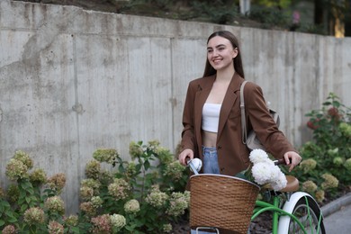 Photo of Woman walking her bicycle with flowers in basket outdoors. Space for text