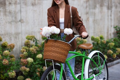 Photo of Woman walking her bicycle with flowers in basket outdoors, closeup