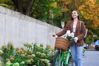 Photo of Woman walking her bicycle with flowers in basket outdoors. Space for text