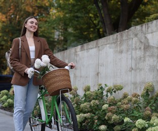 Photo of Woman walking her bicycle with flowers in basket outdoors. Space for text