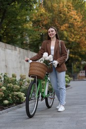 Photo of Woman walking her bicycle with flowers in basket outdoors