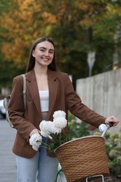 Photo of Woman walking her bicycle with flowers in basket outdoors