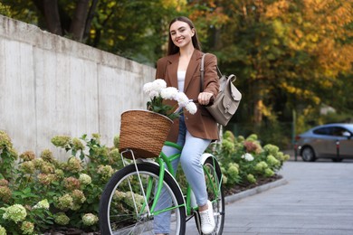 Photo of Woman riding bicycle with flowers in basket on city street