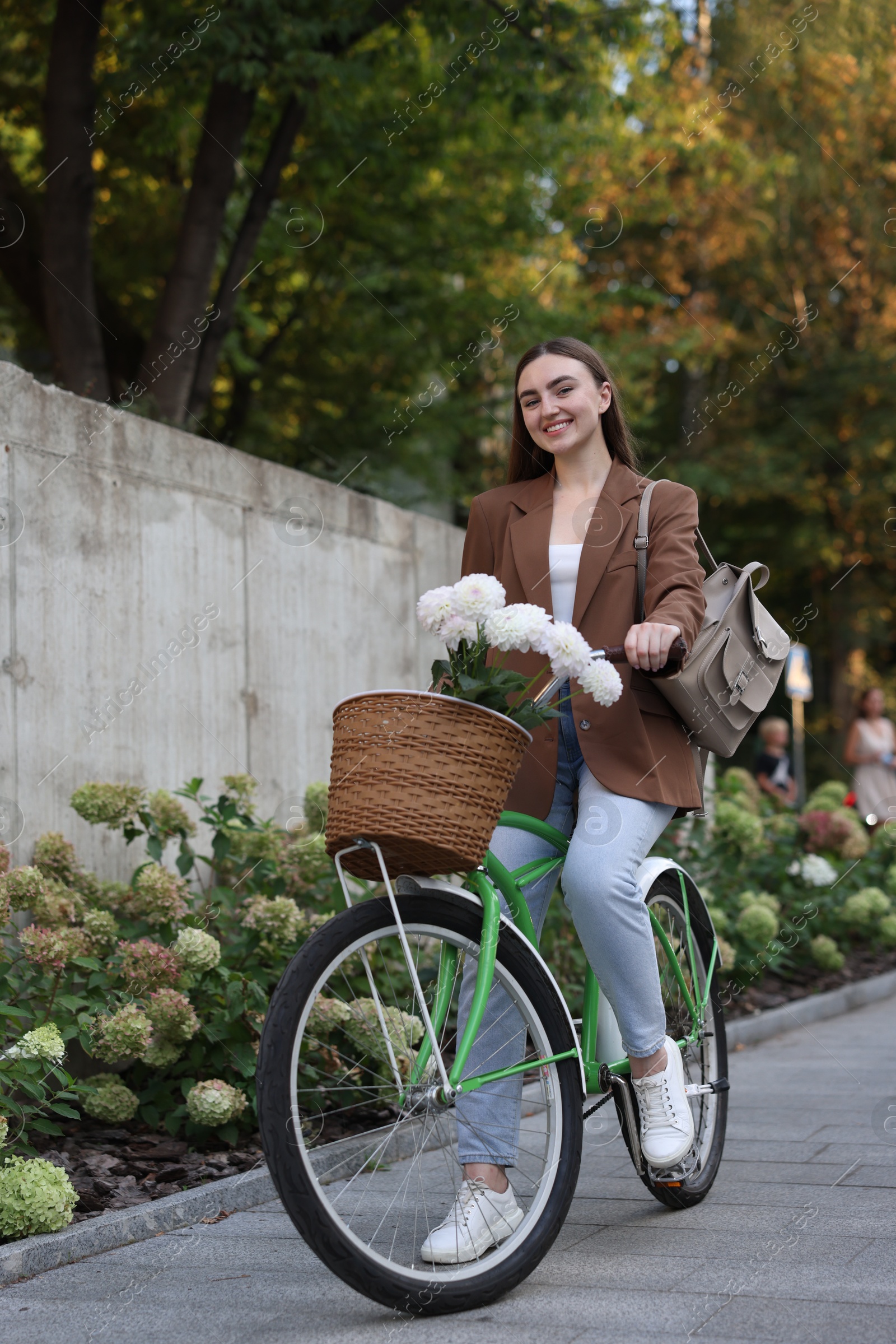 Photo of Woman riding bicycle with flowers in basket on city street