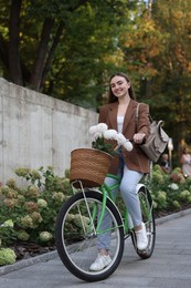 Photo of Woman riding bicycle with flowers in basket on city street