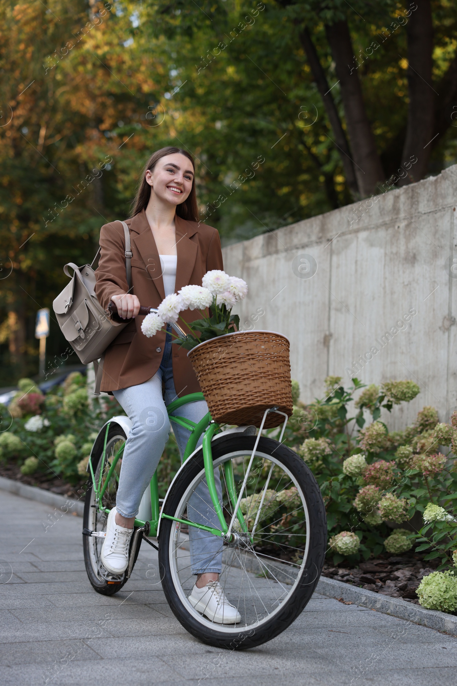 Photo of Woman riding bicycle with flowers in basket on city street