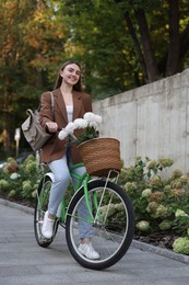 Photo of Woman riding bicycle with flowers in basket on city street