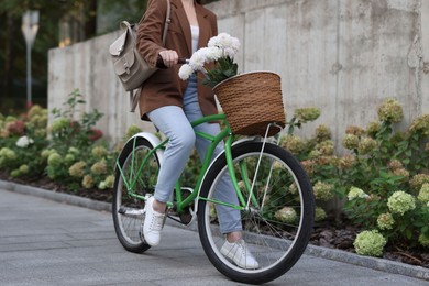 Photo of Woman riding bicycle with flowers in basket on city street, closeup