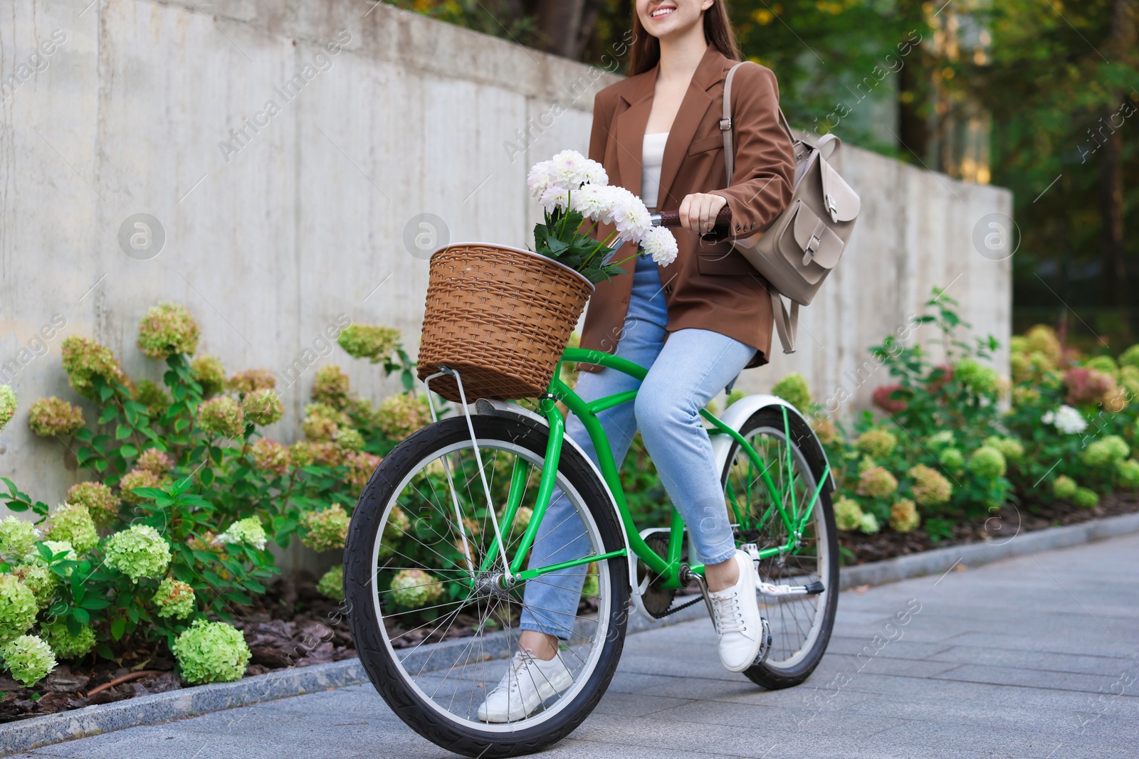 Photo of Woman riding bicycle with flowers in basket on city street, closeup