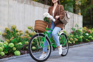 Photo of Woman riding bicycle with flowers in basket on city street, closeup