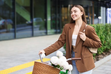 Photo of Woman walking her bicycle with flowers in basket outdoors. Space for text