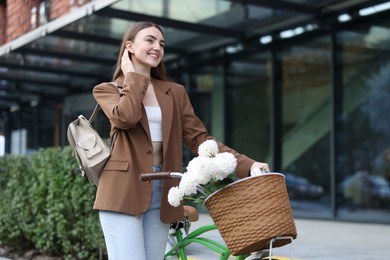 Photo of Woman walking her bicycle with flowers in basket outdoors. Space for text