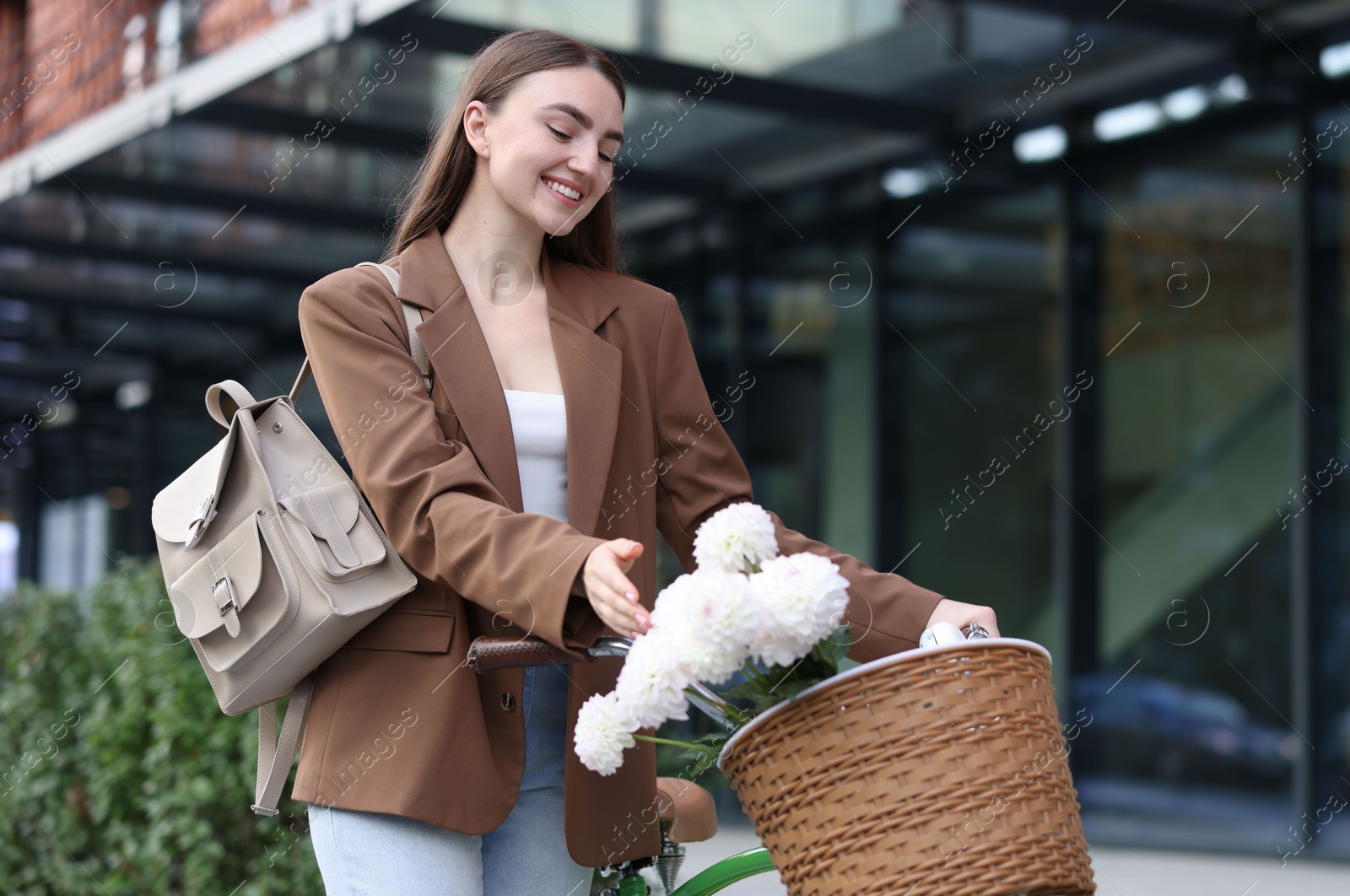 Photo of Woman walking her bicycle with flowers in basket outdoors. Space for text