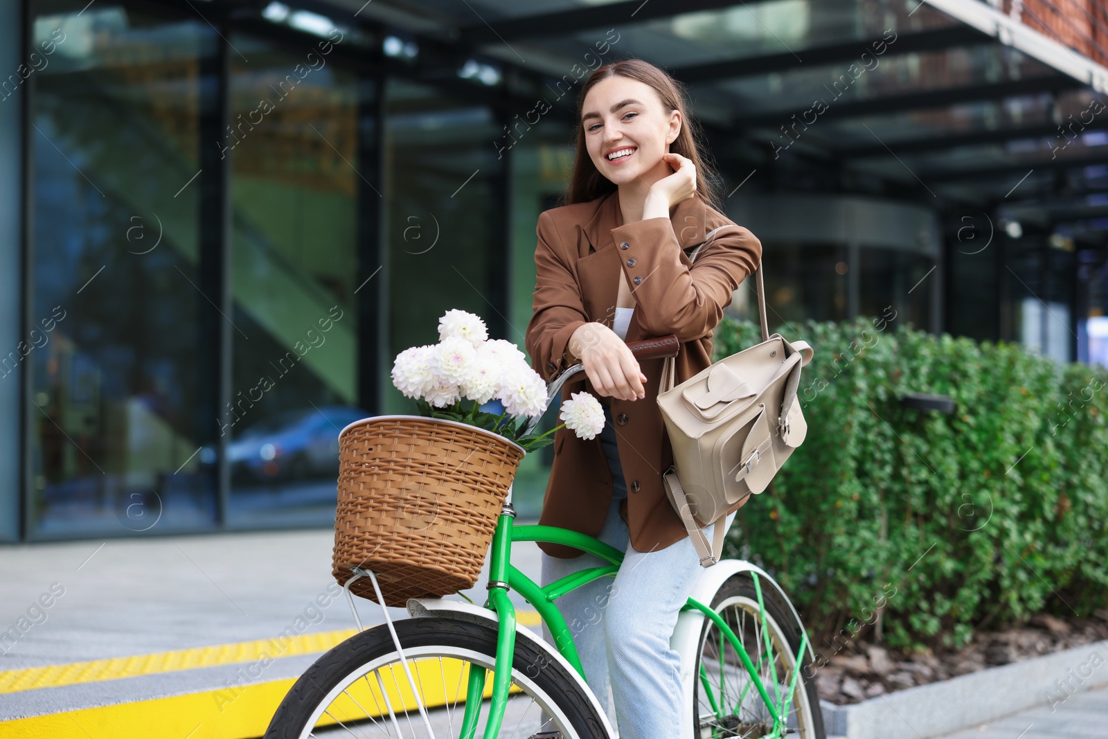 Photo of Woman riding bicycle with flowers in basket on city street