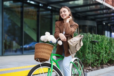 Photo of Woman riding bicycle with flowers in basket on city street