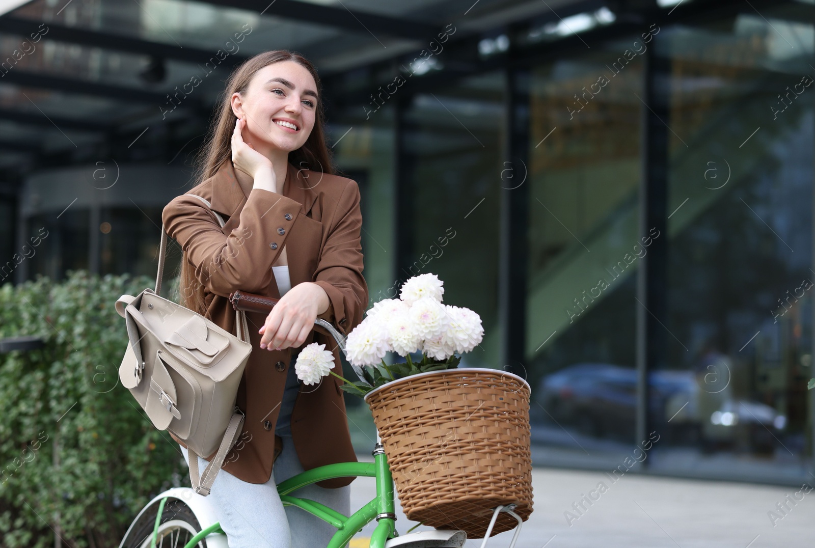 Photo of Woman riding bicycle with flowers in basket on city street. Space for text