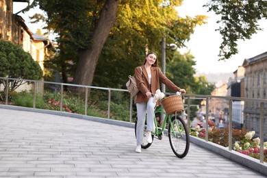 Photo of Woman walking her bicycle with flowers in basket outdoors. Space for text